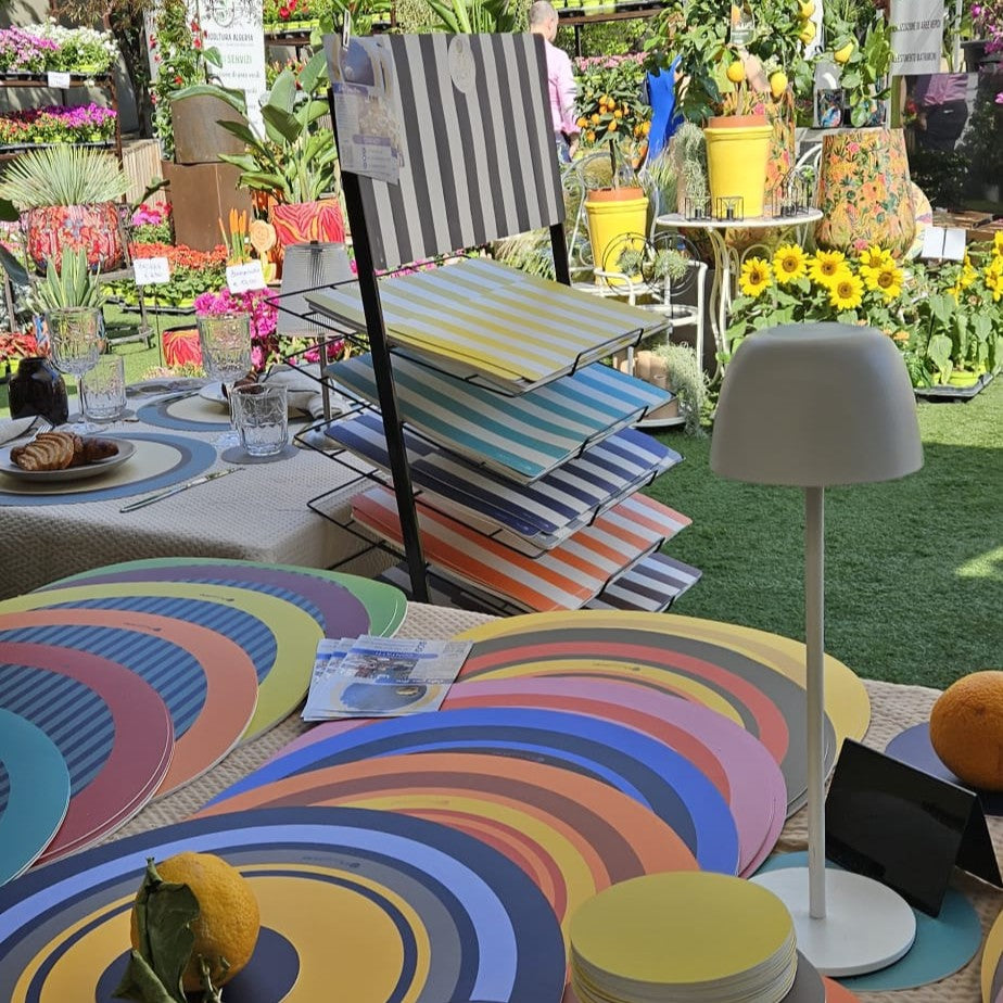 Il banco di It's a little story - Milano: tovagliette rotonde a cerchi colorati e a righe, esposte tra piante e fiori